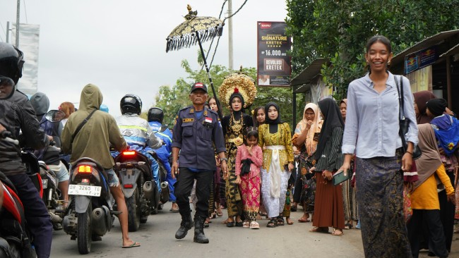 UN_Marco_Dormino.jpg A Sasak bridal procession moves through village traffic, blending tradition and daily life in Lombok, Indonesia. A woman smiles at the camera in the foreground.