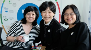 Photo of three GPPAC members sitting in front of an SDG wheel